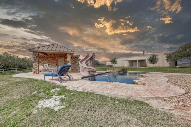 pool at dusk featuring a yard, a patio, and a water slide