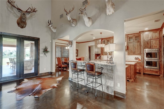 kitchen with french doors, stainless steel double oven, light stone counters, decorative light fixtures, and a breakfast bar area