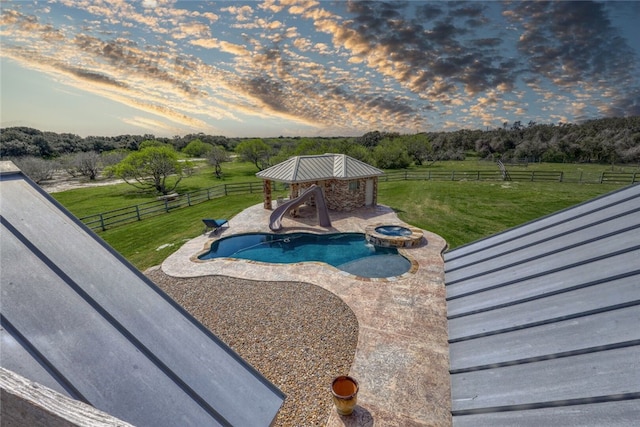 pool at dusk with a patio area, a yard, a water slide, and a rural view