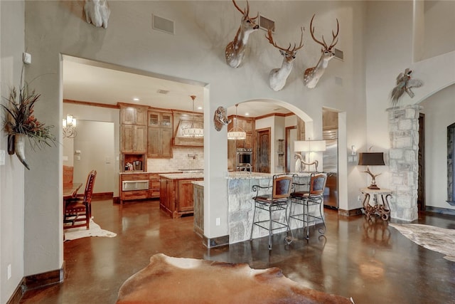 kitchen featuring kitchen peninsula, backsplash, ornamental molding, stainless steel oven, and decorative light fixtures