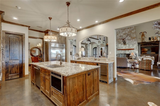 kitchen featuring sink, stainless steel appliances, hanging light fixtures, a stone fireplace, and a center island with sink