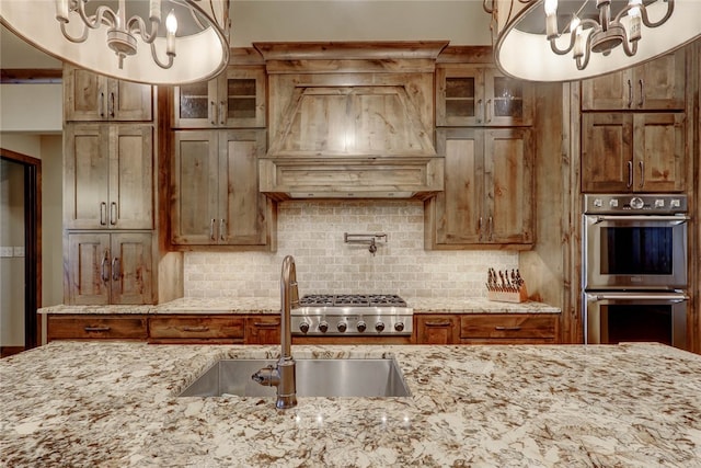 kitchen with light stone countertops, sink, decorative light fixtures, custom range hood, and appliances with stainless steel finishes