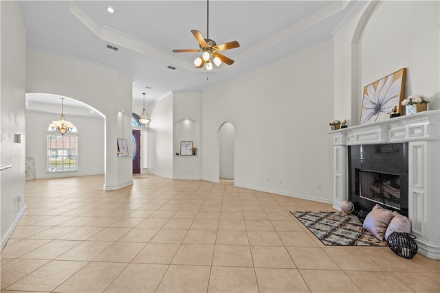 tiled living room with a high end fireplace, ornamental molding, ceiling fan with notable chandelier, a tray ceiling, and a high ceiling