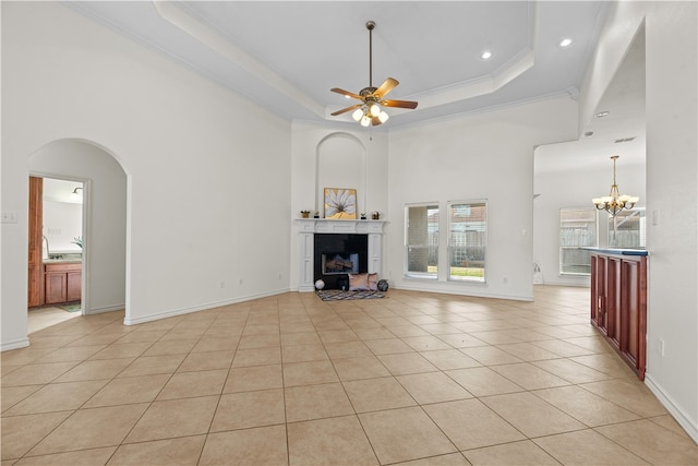 unfurnished living room with a towering ceiling, a tray ceiling, light tile patterned flooring, ceiling fan with notable chandelier, and ornamental molding