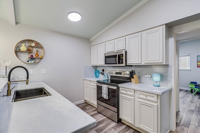 kitchen featuring wood-type flooring, appliances with stainless steel finishes, sink, white cabinets, and lofted ceiling