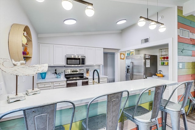 kitchen featuring white cabinetry, appliances with stainless steel finishes, light wood-type flooring, pendant lighting, and lofted ceiling