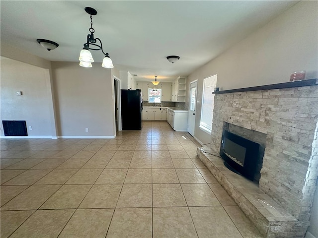 kitchen with white cabinetry, black refrigerator, pendant lighting, a fireplace, and light tile patterned flooring