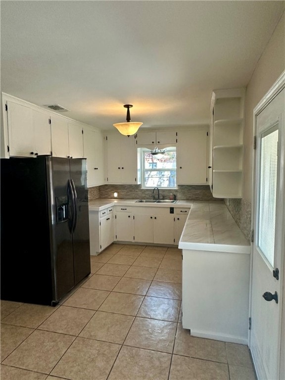 kitchen with white cabinets, black fridge, sink, light tile patterned floors, and tasteful backsplash