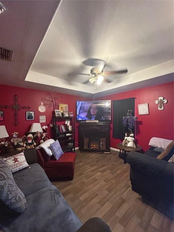 living room with a raised ceiling, ceiling fan, and wood-type flooring