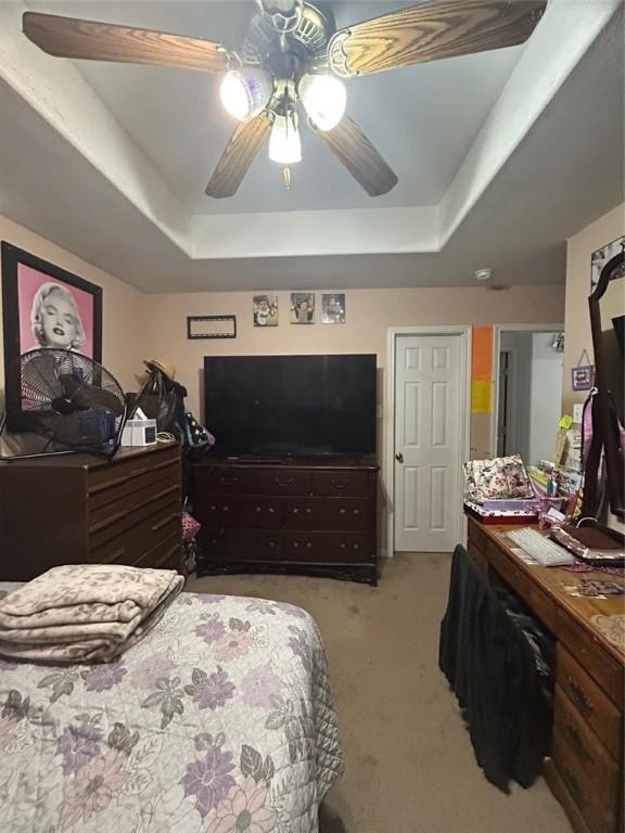 bedroom with ceiling fan, a raised ceiling, and light carpet