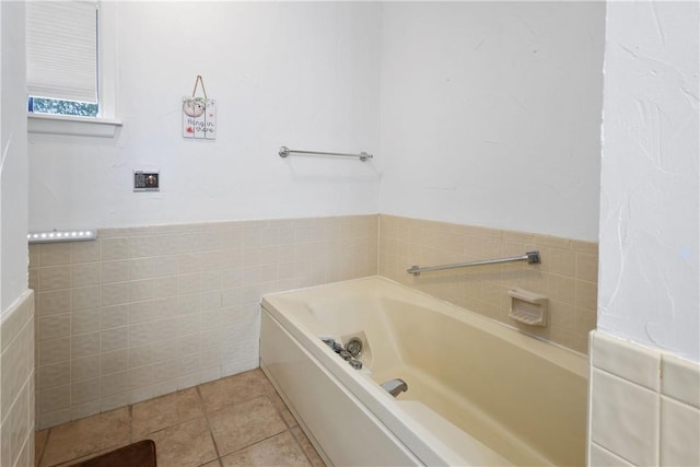 bathroom with a garden tub, tile patterned flooring, a wainscoted wall, and tile walls