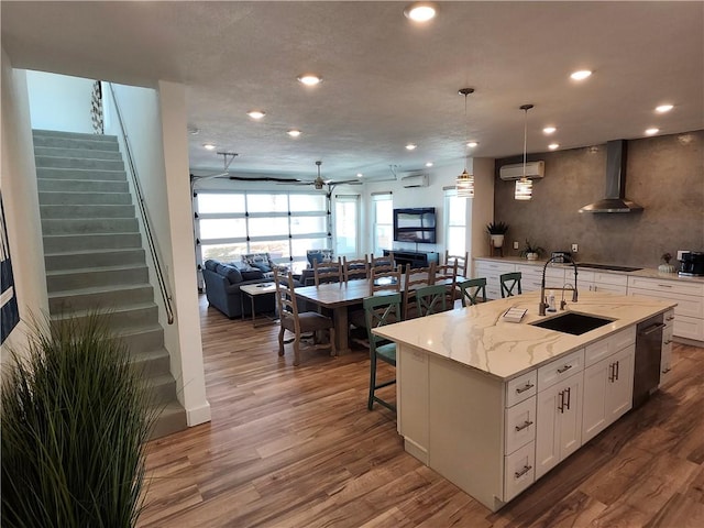 kitchen featuring a wall unit AC, open floor plan, wood finished floors, wall chimney range hood, and a sink