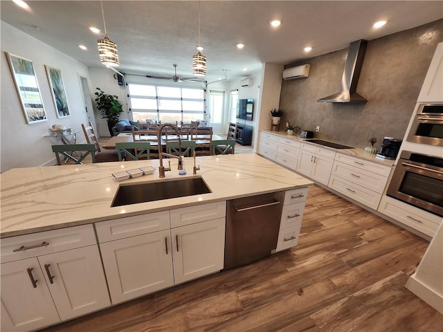 kitchen featuring wall chimney exhaust hood, appliances with stainless steel finishes, open floor plan, an AC wall unit, and a sink