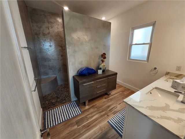 full bathroom with double vanity, baseboards, wood finished floors, a walk in shower, and a sink