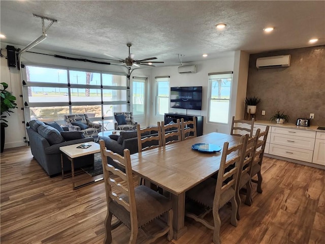 dining space featuring a wall unit AC, light wood-type flooring, and a textured ceiling