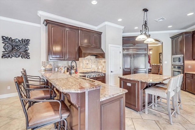 kitchen with visible vents, a kitchen bar, under cabinet range hood, arched walkways, and built in appliances