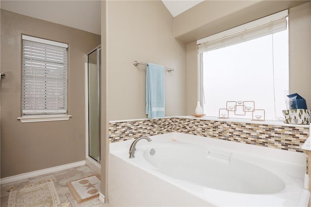 bathroom featuring a stall shower, a garden tub, and baseboards