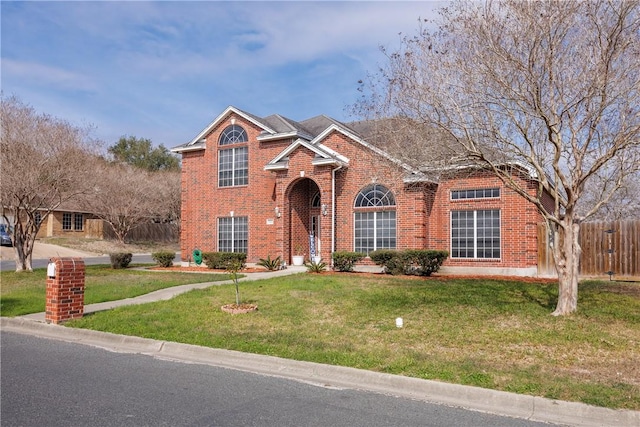 traditional-style home featuring brick siding, a front yard, and fence