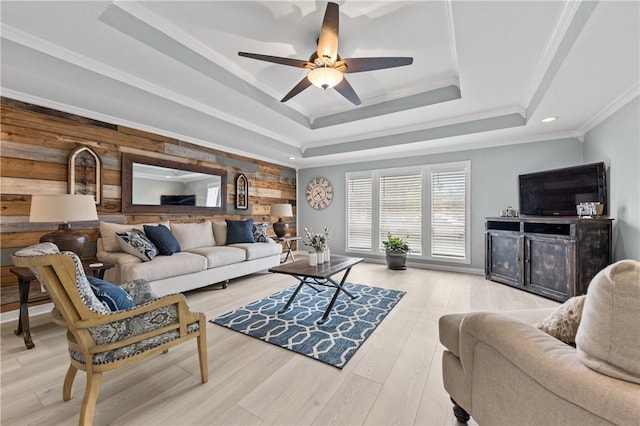 living room with a tray ceiling, wood walls, light hardwood / wood-style flooring, and ornamental molding