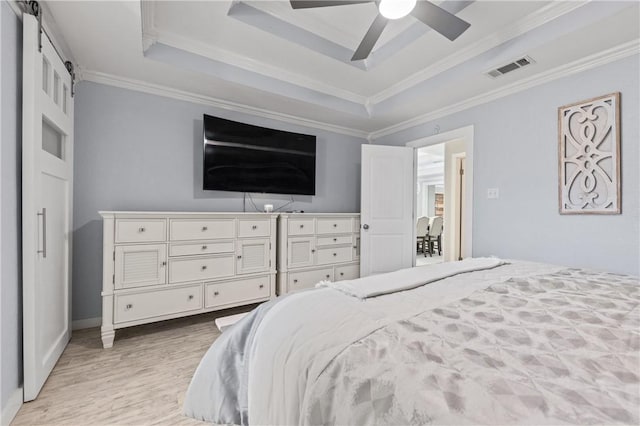 bedroom with a raised ceiling, ceiling fan, crown molding, a barn door, and light hardwood / wood-style floors