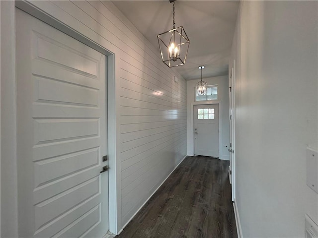 doorway featuring wooden walls, a notable chandelier, baseboards, and dark wood-style flooring