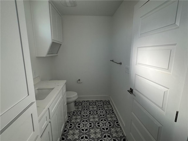 half bathroom with baseboards, toilet, vanity, and tile patterned flooring