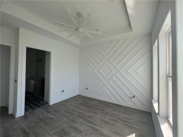 unfurnished bedroom with dark wood-type flooring, ceiling fan, baseboards, a tray ceiling, and ensuite bathroom