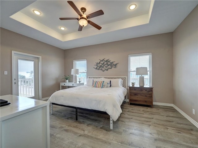 bedroom featuring a raised ceiling, ceiling fan, access to exterior, and light wood-type flooring