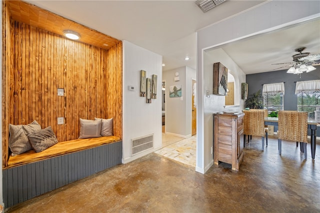 interior space featuring ceiling fan, wooden walls, and concrete floors