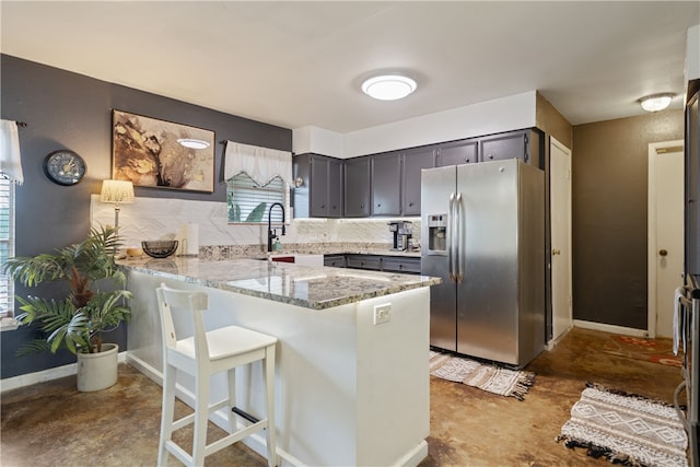 kitchen featuring sink, light stone counters, stainless steel fridge with ice dispenser, decorative backsplash, and kitchen peninsula