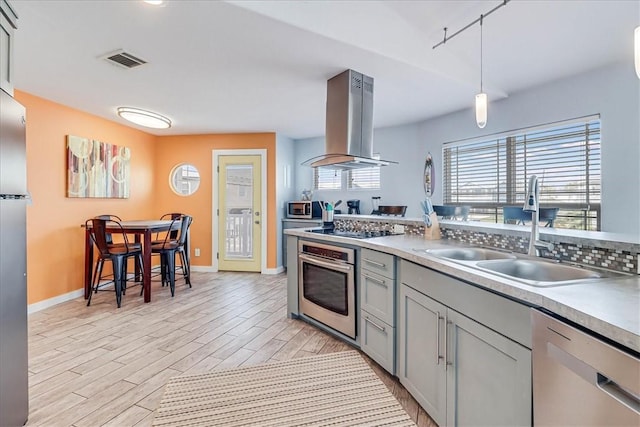 kitchen with pendant lighting, sink, wall chimney exhaust hood, appliances with stainless steel finishes, and light hardwood / wood-style floors