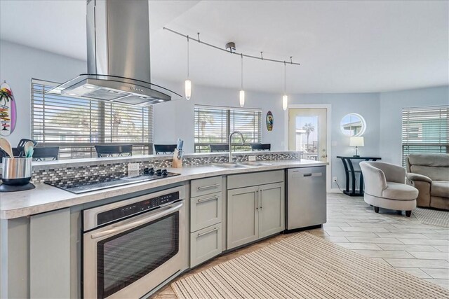 kitchen with appliances with stainless steel finishes, island range hood, sink, decorative light fixtures, and gray cabinets