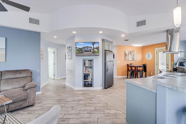 interior space featuring sink, hanging light fixtures, vaulted ceiling, stainless steel fridge, and light wood-type flooring