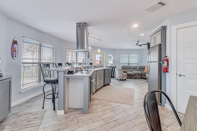 kitchen with a kitchen breakfast bar, gray cabinetry, an island with sink, and a healthy amount of sunlight