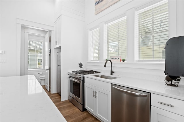 kitchen featuring white cabinets, appliances with stainless steel finishes, dark wood-type flooring, light countertops, and a sink