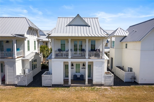 rear view of house featuring a balcony, a standing seam roof, metal roof, and a lawn