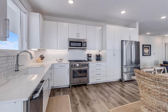 kitchen featuring high quality appliances, white cabinetry, sink, and light wood-type flooring