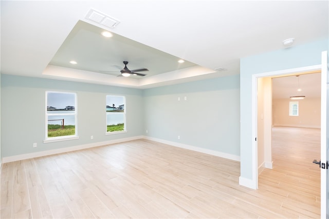 empty room featuring ceiling fan, light hardwood / wood-style floors, and a raised ceiling