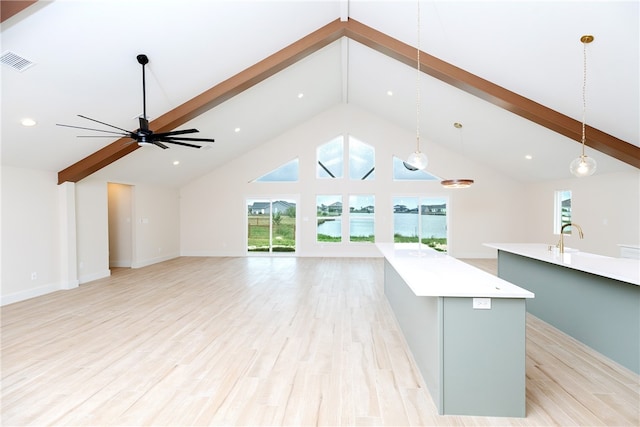 kitchen with light wood-type flooring, decorative light fixtures, an island with sink, and beam ceiling