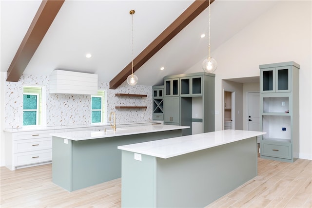 kitchen featuring light hardwood / wood-style floors, white cabinetry, a center island with sink, pendant lighting, and lofted ceiling with beams