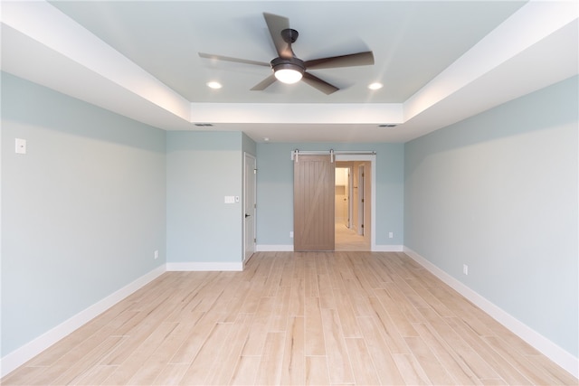 spare room featuring light wood-type flooring, a barn door, ceiling fan, and a tray ceiling