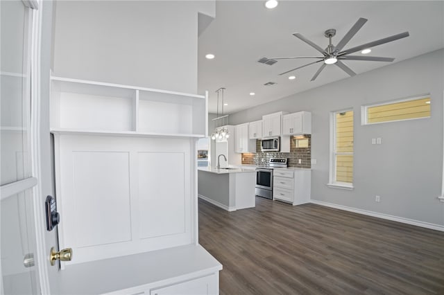 kitchen featuring stainless steel appliances, white cabinetry, dark hardwood / wood-style flooring, hanging light fixtures, and an island with sink