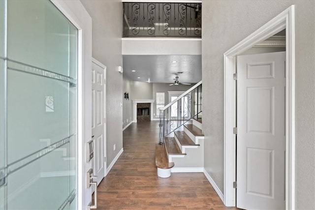 foyer featuring ceiling fan, a fireplace, wood finished floors, baseboards, and stairs