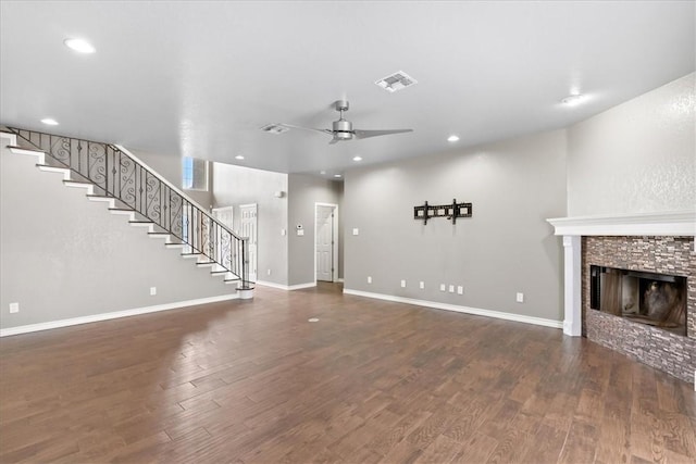 unfurnished living room featuring ceiling fan, a stone fireplace, wood finished floors, visible vents, and stairs