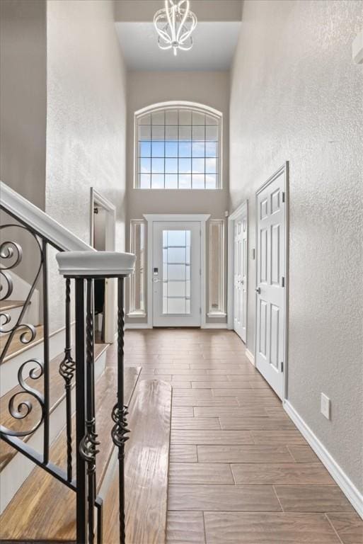 foyer entrance with baseboards, a textured wall, an inviting chandelier, wood tiled floor, and stairs