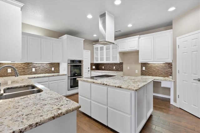 kitchen featuring double oven, black electric cooktop, a sink, white cabinetry, and island exhaust hood