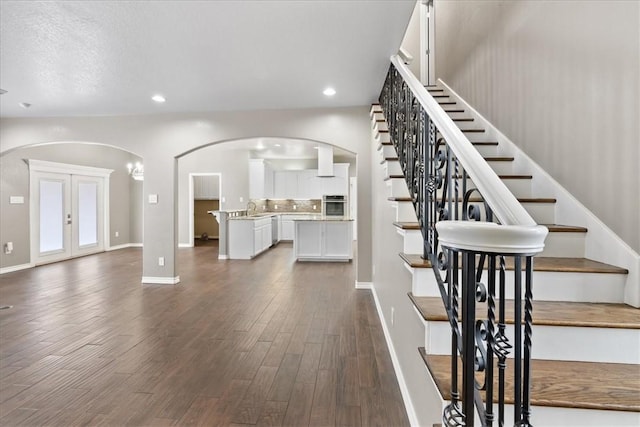 interior space with arched walkways, french doors, wood finished floors, and recessed lighting