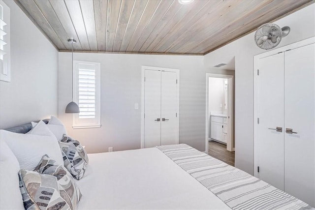 bedroom featuring ensuite bath, multiple closets, and wooden ceiling