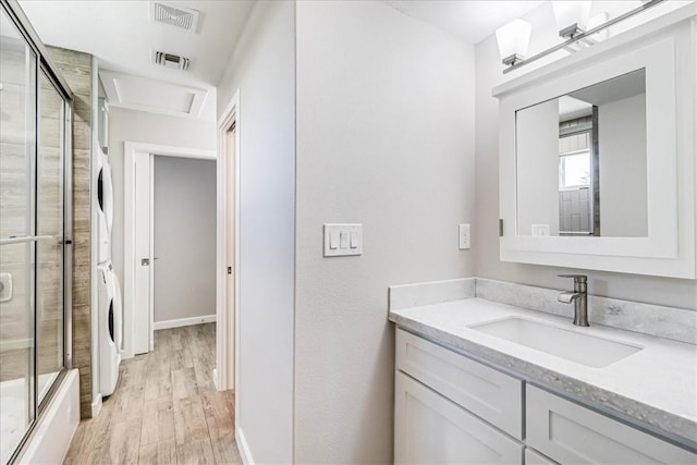 bathroom with hardwood / wood-style floors, vanity, stacked washer / dryer, and a shower with shower door