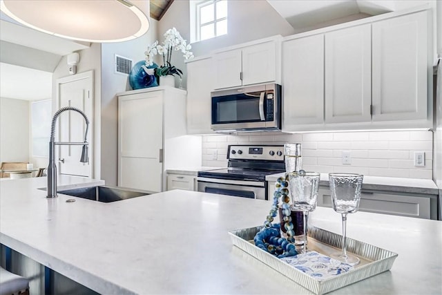 kitchen with sink, vaulted ceiling, decorative backsplash, white cabinetry, and stainless steel appliances